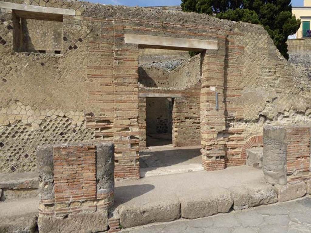 II.2 Herculaneum, October 2014. Looking west towards doorway. Photo courtesy of Michael Binns.
According to Pagano, “Although this has not been totally uncovered, at least one can judge that this would have been a large dwelling, and was given this name by the finding of a fresco showing the shepherd Argo who protects the nymph Io. On the outside we see two long benches at the side of the door, in front of which the masonry pilasters covered in stucco held up a roof. This door, as well as in the preceding house, was not the main entrance but knowing the manner of building/construction of the ancients, this must have been found on the opposite side which is not yet excavated.
Firstly, it presents a room somewhat preserved with beautiful walls painted in red with architectural drawings and pictures of marine views. The floor is in white mosaic, with large window on the left protruding over the garden.
The garden or peristyle has a beautiful colonnade around which held the roof of the portico. Several of the columns still retain their capitals of white stucco very well worked with taste.
Around the portico there are many rooms, and the one seen in the first portico on the left entering, with walls painted in red and floors of white mosaic, called an exedra or reception room which was without doors, and according to the use of the ancients, would have been closed with a curtain of cloth.
Another large room for the same use seen in the portico on the right, which was also decorated with paintings and marble floor. Presently, there are just traces remaining. Then, you go to another room for dining with large window protruding to the garden. It has walls painted in red and architectural designs”.
See PAGANO, N, Descrizione degli scavi di Ercolano, 1870. (p.22-25)