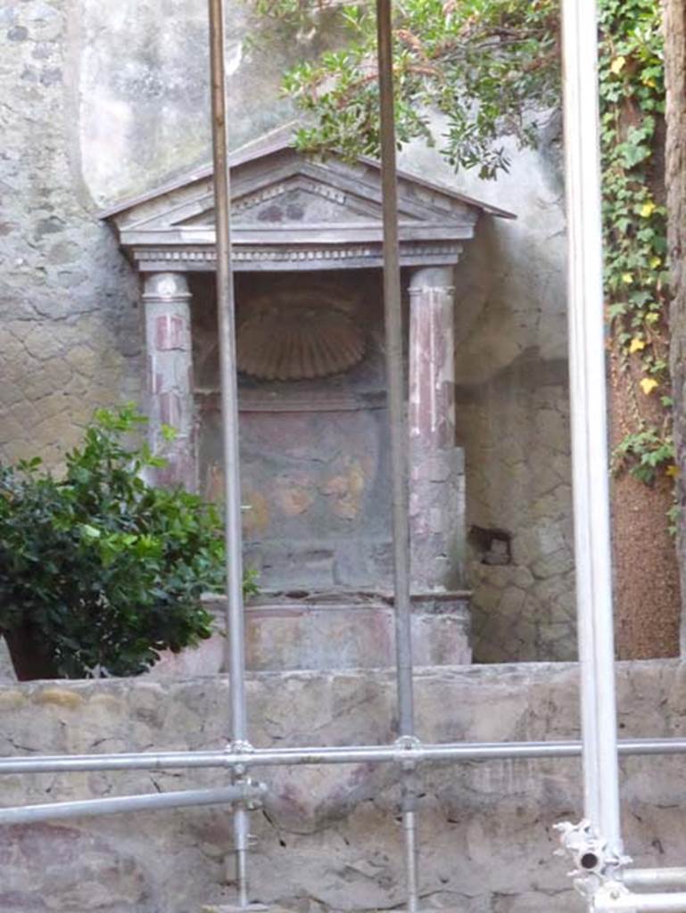 Ins. V 5, Herculaneum, September 2015. Looking from window of tablinum towards garden and shrine. The little courtyard, closed all around by a parapet and paved in opus signinum was chiefly designed to carry away the rainwater to the cistern.
It was decorated with an aedicula lararium.