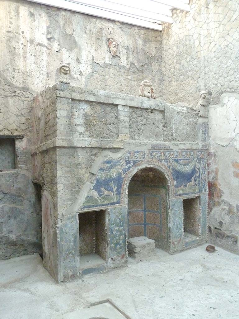 V.7 Herculaneum, September 2015. 
North wall with nymphaeum which is covered with glass paste mosaic with shells, and with theatrical masks above.
The tank that fed the fountain is above the niche. 
