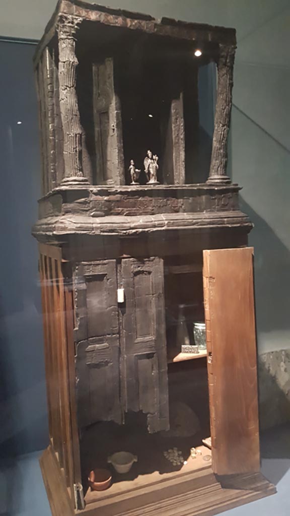 V.31 Herculaneum, August 2023. 
Wooden cupboard, with its upper part in the form of a tiny temple.
This was found in Room 2 in 1934, the room on the right of the entrance corridor.
On display in exhibition entitled – “Materia. Il legno che non bruciò ad Ercolano”.  
Photo courtesy of Maribel Velasco.

