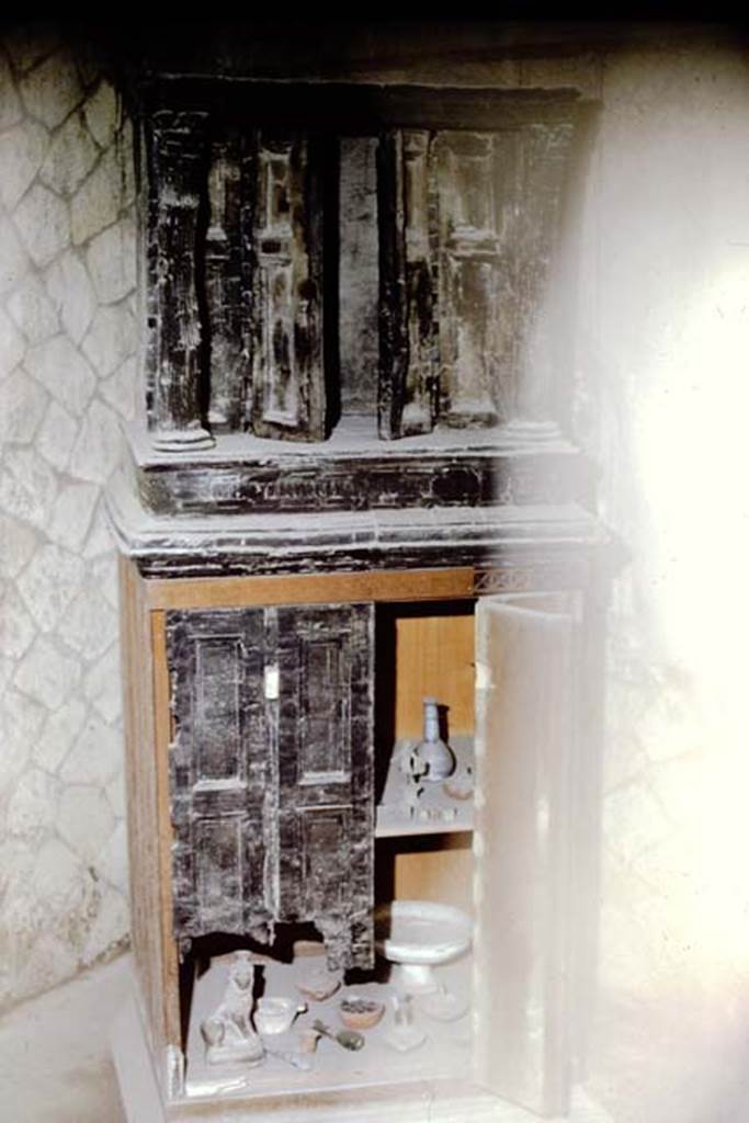 Ins.VI.13, Herculaneum, 1961. Wooden lararium with marble capitals. Photo by Stanley A. Jashemski.
Source: The Wilhelmina and Stanley A. Jashemski archive in the University of Maryland Library, Special Collections (See collection page) and made available under the Creative Commons Attribution-Non Commercial License v.4. See Licence and use details. J61f0591
According to Deiss, found in the black saloon” was another miraculous wooden survival:  a shrine in the form of a miniature temple. The fluted columns were of wood, the capitals of marble. Preserved within are the statuettes typical of a lararium maintained by people who remained devout in the old Roman faith”.
See Deiss, J.J. (1968). Herculaneum: a city returns to the sun. U.K, London, The History Book Club, (p.64)
