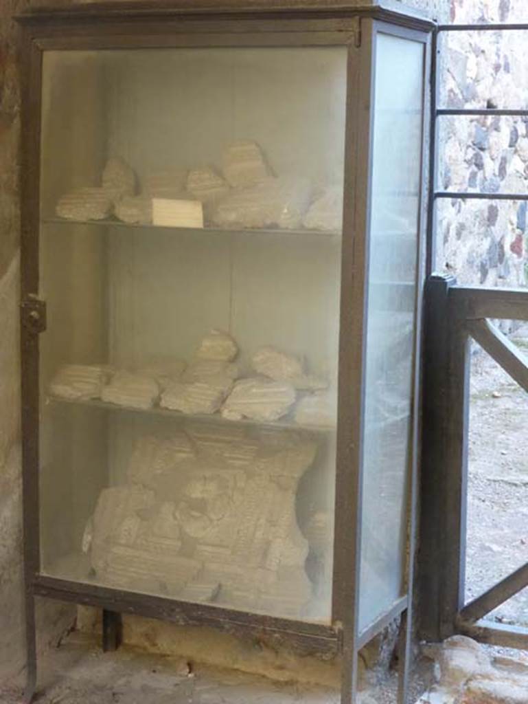 VI.16 Herculaneum. September 2015. One of the ancient glass display cabinets placed at Herculaneum by Maiuri. Now containing some fragments of stucco belonging to the four-sided arch opposite the shop, on the north side of Decumanus Maximus.