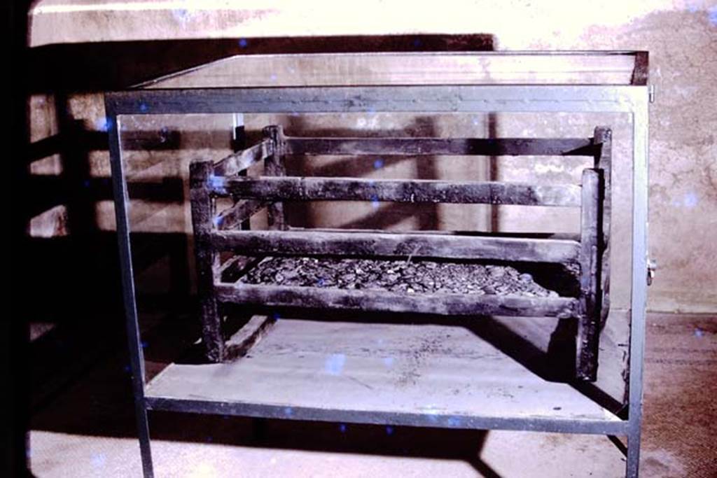 Ins. Orientalis I, 1, Herculaneum, 1975. Cradle or crib. Photo by Stanley A. Jashemski.   
Source: The Wilhelmina and Stanley A. Jashemski archive in the University of Maryland Library, Special Collections (See collection page) and made available under the Creative Commons Attribution-Non Commercial License v.4. See Licence and use details. J75f0700
According to Deiss a cradle was found in the House of the Gem, but as originally this was linked to the House of M. Pilius Primigenius Granianus, it is probably the same one and over time the location has become muddled.  This photo may or may not even be of the same carbonized wooden cradle.
Deiss said, (talking about the House of the Gem) – 
“The rooms were notable for their decoration before being stripped by the Bourbons. A superior mosaic floor of geometric design somehow was overlooked in the dining room. Also missed was a cradle containing an infant’s bones – though it seems incredible that a baby could have been abandoned to the mud”.  
See Deiss, J.J. (1968). Herculaneum, a city returns to the sun. London, The History Book Club, (p.44)
