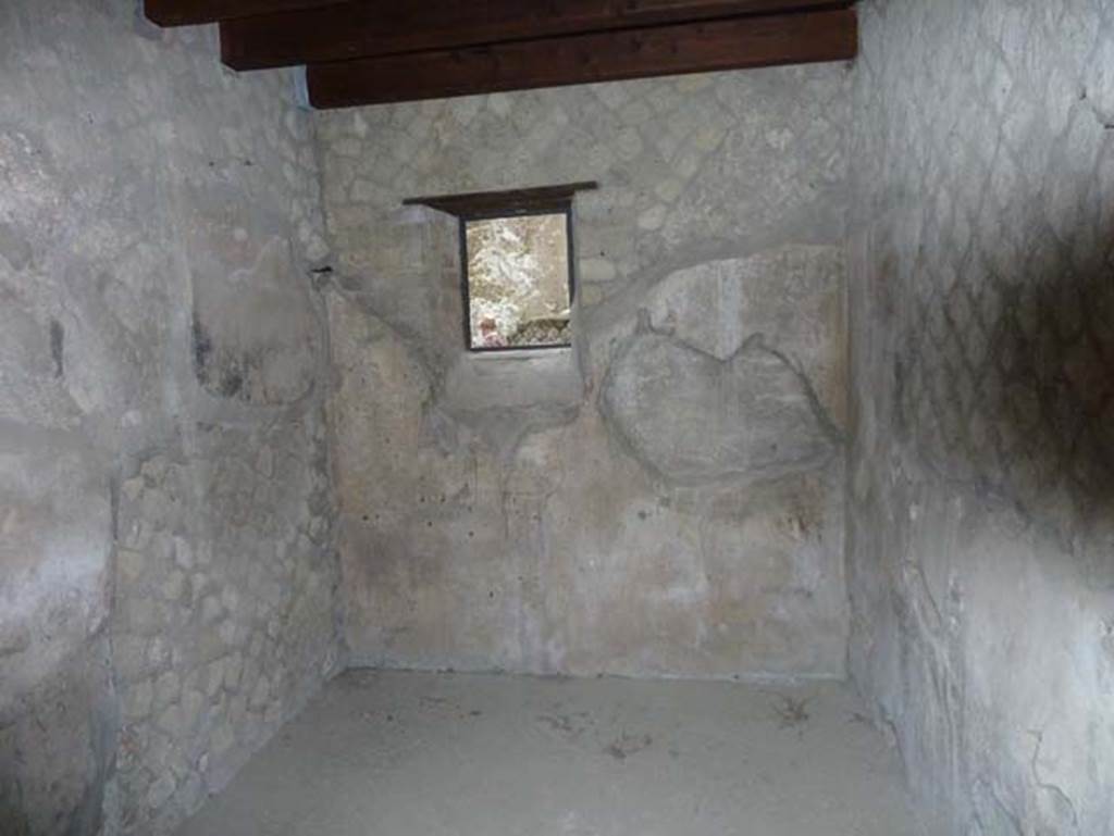 Ins. Orientalis II.10, Herculaneum. September 2015. Looking east in cubiculum (a) with window in east wall.  This is the room that a skeleton was found on a bed, according to the excavation diaries. Nowadays, the room is bare, and the items presumably locked away in the deposits, or sent to Naples Museum.
Wallace-Hadrill writing in his book shows a deep admiration for Maiuri and his aim of promoting Herculaneum as a “living museum”. However he does point out that Maiuri felt no qualms in dressing his “museum areas” on view to the publlc with items that told a good story, but were not necessarily found there. For example, in this house is the room of the so-called embroidery girl, the ricamatrice, whose teenage skeleton was found lying on the bed (according to Maiuri – the adolescent victim of who knows what cruel or anguishing abandonment): by her bed is her embroidery frame and a little inlaid stool, as well as a bronze candelabrum and a marble table. But careful examination of the actual excavation records for summer 1936 suggests that by the time, twenty years later, he was writing this up for publication, he had either lost track of the actual records or ceased to care, and was more interested in publishing the “open museum” he had so ingeniously constructed. One major fraud has been mentioned before (p.83). The little weaving girl, is alas, pure myth. The excavation diaries do indeed record a skeleton on the bed, but it is that of a young man. But this apart, there were no finds. The wooden stool came from the house opposite, the loom and candelabrum from heaven knows where. It looked great for the public.  See Wallace-Hadrill, A. (2011). Herculaneum, Past and Future. London, Frances Lincoln Ltd., (p.278)
On page 83 he wrote, in the case of the ‘weaving girl’ Maiuri’s passion for a good story evidently carried him away. As displayed to the public, the backroom of the shop contained the skeleton of a teenage girl lying on a couch. By her couch is a little loom, on which she was weaving before the eruption, a small stool with marquetry decoration in front of it for her to work from. A small marble table rests against the left-hand wall, and a bronze candelabrum provides illumination on the right. The excavation diaries tell a very different story. They report the bed and skeleton of a ‘young boy’ and otherwise ‘no finds’. Maiuri has carefully put together this composition, and the entire story of the weaving girl. Deeply touching, but not actually true.  See Wallace-Hadrill, A. (2011). Herculaneum, Past and Future. London, Frances Lincoln Ltd., (p.83)


