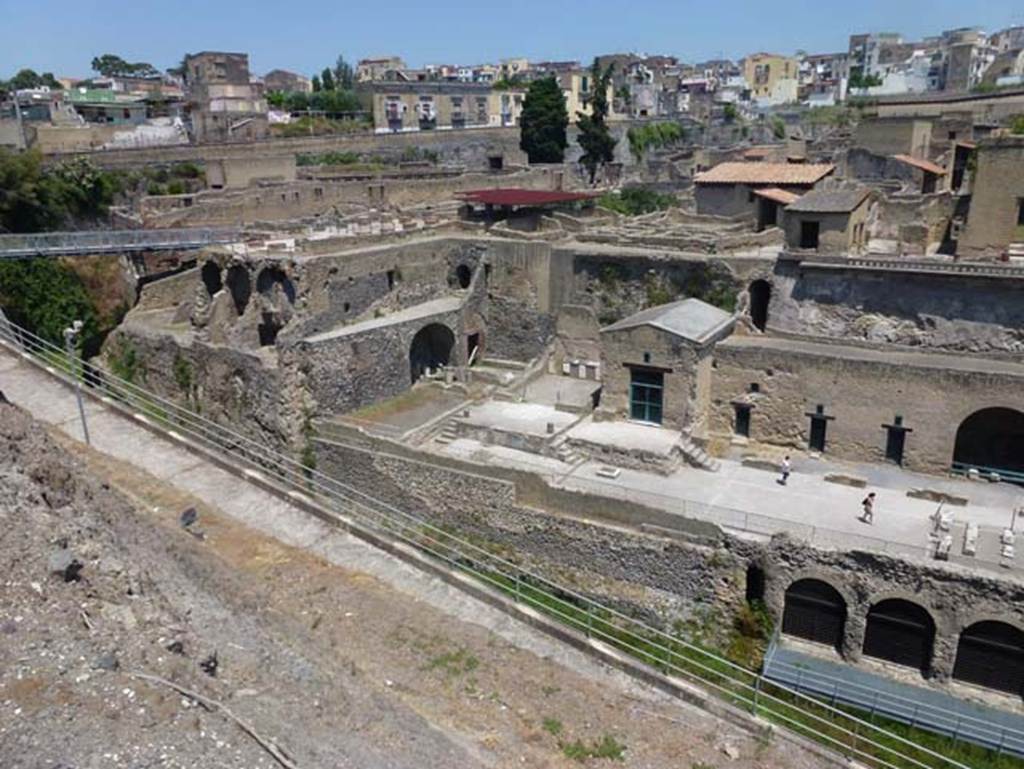 Herculaneum, June 2012. Looking north-west towards Sacred Area, below the town walls.
The steps to a podium, in the centre, leads to a podium outside the doorway into the Shrine of Venus.
On the left side of it, are more steps to another podium outside the Shrine of the Four Gods. Photo courtesy of Michael Binns.
According to Wallace-Hadrill –
“One of the benefactions of the great Nonius Balbus to his town was to repair the walls.
We can see how he monumentalized the southern wall towards the sea, encasing it in a ‘network’ technique of opus reticulatum that was standard in the period of Augustus (see page 22).
He may also have helped to improve the terraces beneath the walls.
In any case, his statue and funerary altar were given pride of place on one of them by the entrance to the Suburban Baths.
To the west, there had already, probably since the second century BC, been a small temple, of which the podium has been glimpsed in an excavation.
This may be the temple of the goddess Herentas Erycina, the Oscan cult name of Venus, which is mentioned in the one surviving inscription in Oscan.
It was replaced, perhaps as part of Balbus’ programme, by two small temples, probably both dedicated to Venus.
Four handsome reliefs in the style of early Greek sculpture, showing the gods Minerva, Mercury, Neptune and Vulcan, do not necessarily indicate who was worshipped.”
See Wallace-Hadrill, A. (2011). Herculaneum, Past and Future. U.K, London, Frances Lincoln Ltd., (p.166).