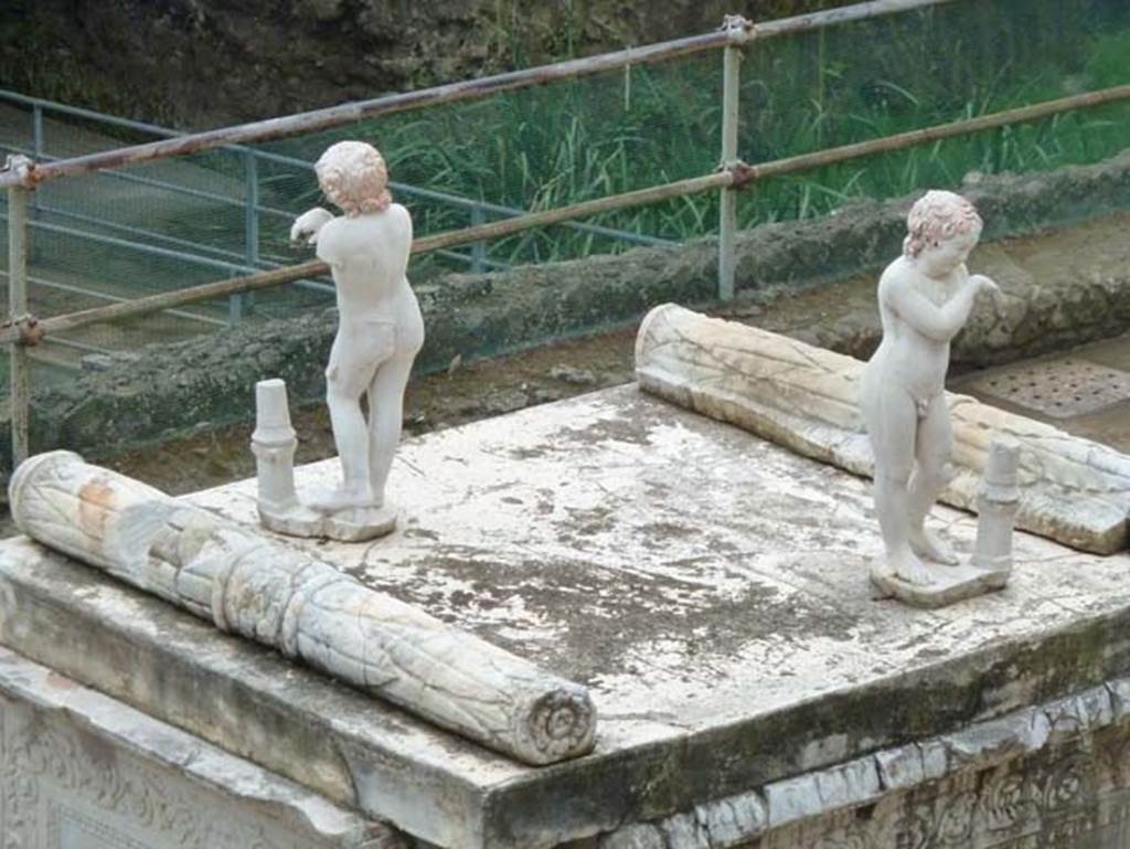 Herculaneum, September 2015. On the top of the altar stand two marble statues of sleeping funeral figures which would have been leaning on torches, but are now ruined. One of the two statues shows considerable traces of red-lead colour on their head of hair.
