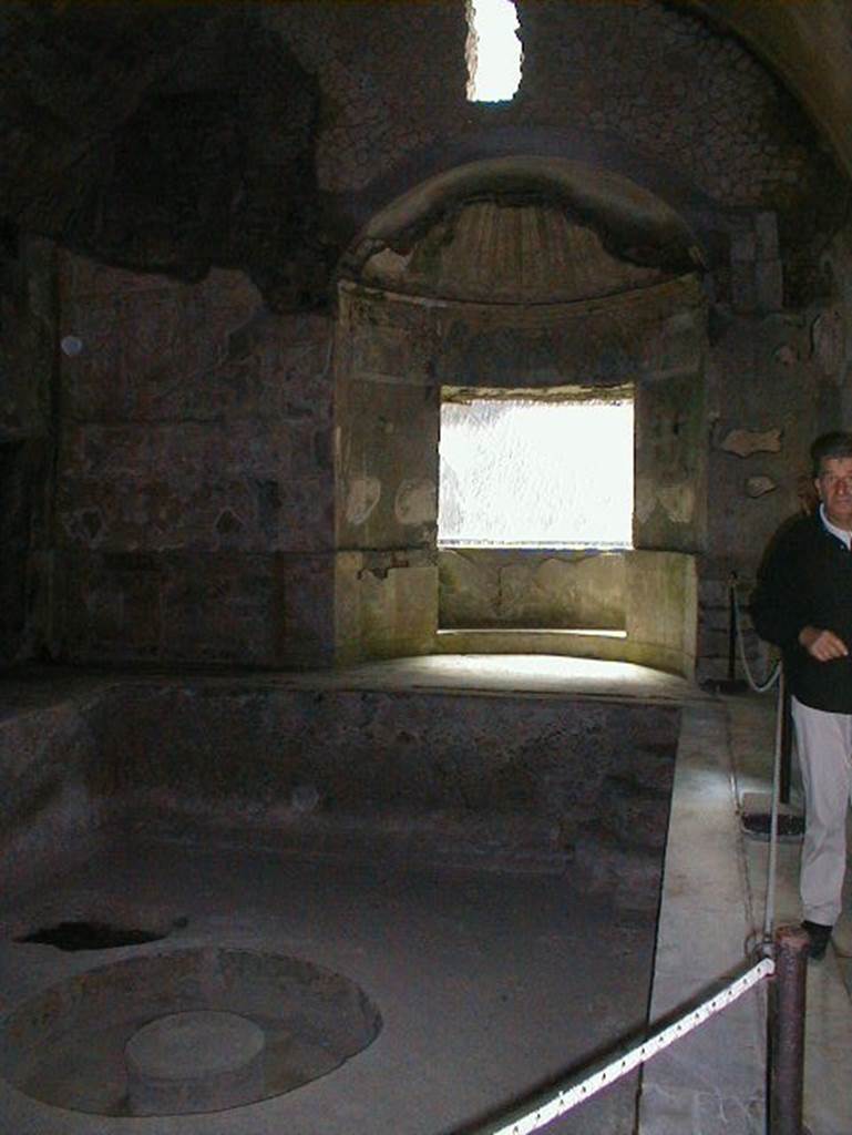 Suburban Baths, Herculaneum, May 2004. Second Caldarium, with large central bath and window overlooking the sea. Looking east. According to Wallace-Hadrill,
The original Baths were built with the standard areas of entrance hall, followed by cold, warm and hot rooms. This original Caldarium was small and intimate.
Then a second Caldarium was added, with its own furnace operating by direct heating immediately under the bronze “samovar” in the middle of the pool.
It offered an area of warm water big enough for up to twenty to swim in. 
See Wallace-Hadrill, A., (2011): Herculaneum, past and future. London, Francis Lincoln Ltd., (p.159).

