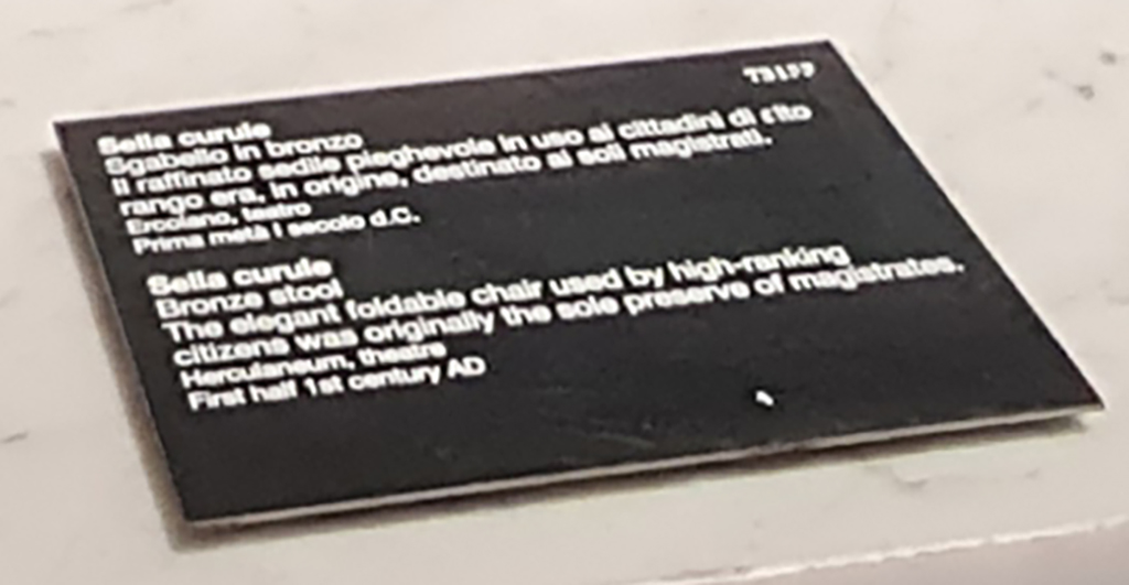 Herculaneum Theatre. April 2023. Descriptive card. Second bronze stool. Sella curule.
Scheda descrittiva. Sella curule. Sgabello in bronzo.
Photo courtesy of Giuseppe Ciaramella.