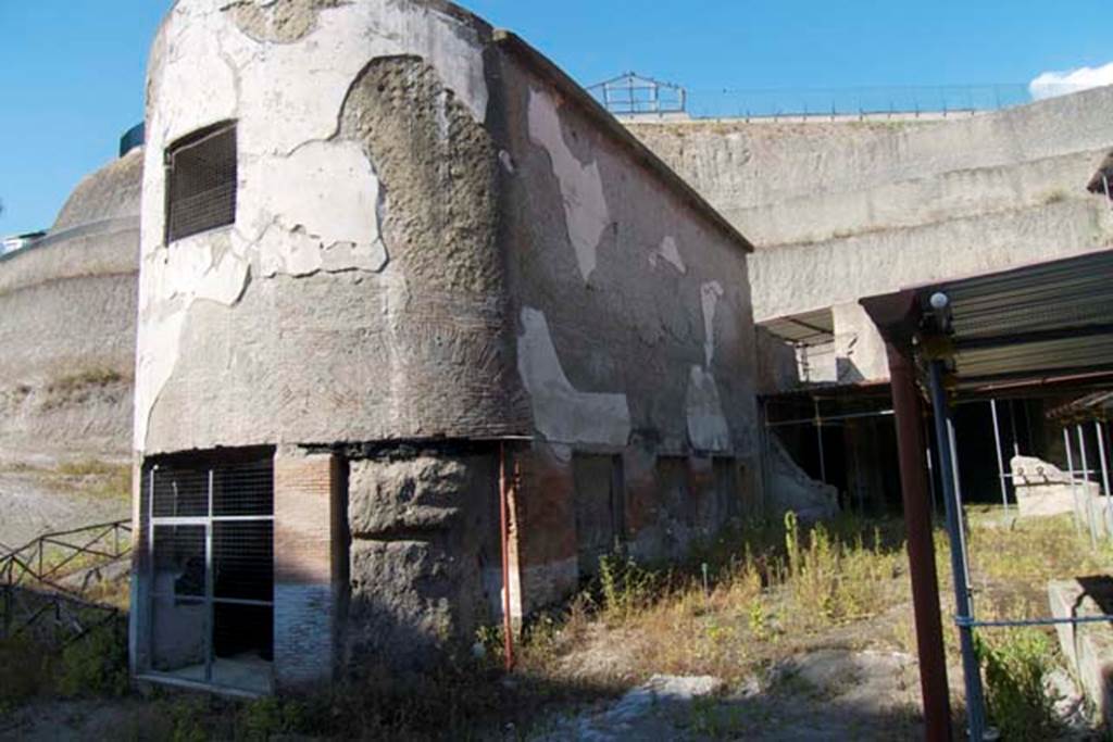 South-western baths, Herculaneum. July 2010.
Looking towards baths complex 1, on left, separated by the adjacent terrace 2, with the lower level of large residential property, on right.
Photo courtesy of Michael Binns.
The three windows with their pyroclastic materials on the south side can be seen.
In the semi-circular apse, there would have been another three windows.
In the upper wall of the apse was a smaller rectangular window for light.
There were another three windows on the north side.
The terrace would have been bordered on the south and east by a portico, with flooring of cocciopesto with white tesserae dots.