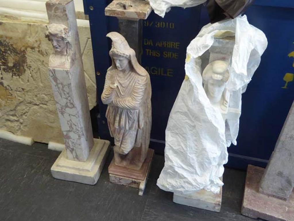 III.11 Herculaneum, September 2016. Statuette of Atthis, (centre). Photo courtesy of Michael Binns.
According to a photo on page 58 of Maiuri’s book, this statuette was photographed in front of a table, near the north wall of room 2.
The wording on page 59 suggests that this table was actually found in an upper room of the house.
“E per quanto la casa fosse stata abilmente frugata con cuniculi e gallerie per ogni lato, era miracolosamente sfuggita ai ricercatori borbonici, da un ambiente del piano superiore, una preziosa mensa in marmo epirota (molossium), sostenuta da un trapezoforo effigiato in forma di Atthis, il piu bello esempio che si abbia di tal genere di mense figurate, fra quante ce ne ha restituite il sottosuolo di Pompei.”
(trans: And so far as the house had been ably ransacked with tunnels and galleries on each side, found from an upper-floor room was a precious table in Epirote marble (Molossium), supported by a single table support in the image of Atthis, which had miraculously escaped the Bourbon searchers - the most beautiful example that you have of this kind of genere of figured table, among the many we have recovered from the underground of Pompeii.) 
See Maiuri, A. (1932). “Ercolano”. Italy, Novara. Istituto Geografico De Agostini, (p.58 and 59).
