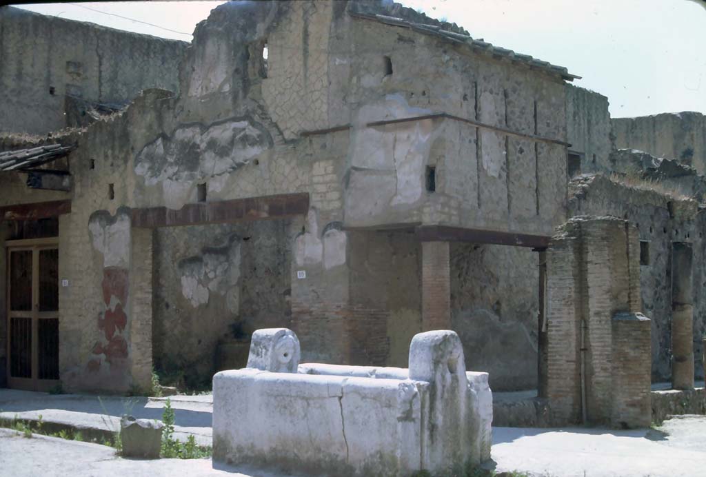 V.10/9 Herculaneum. 7th August 1976. Looking south-east from Decumanus Maximus across fountain towards corner of Insula V. 
Photo courtesy of Rick Bauer, from Dr George Fay�s slides collection.
