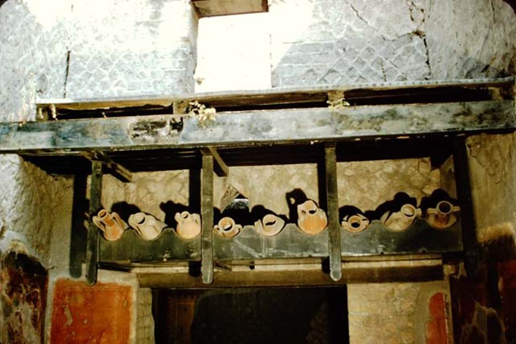 Ins. Orientalis II.9, Herculaneum. 1957. Detail of supporting wooden scaffold containing amphorae. 
Photo by Stanley A. Jashemski. 
Source: The Wilhelmina and Stanley A. Jashemski archive in the University of Maryland Library, Special Collections (See collection page) and made available under the Creative Commons Attribution-Non Commercial License v.4. See Licence and use details.
J57f0452
Note: in 1957, the carbonised wooden ladder was not on display.
According to Cooley and Cooley, an inscription was found on an amphora fragment in the bar belonging to M. Livius Alcimus, this bar at Ins. Or. II.9, along with other amphorae found labelled as his property. 
The inscription translated as –
Excellent Coan vintage at Herculaneum of Livius Alcimus.     (CIL IV 10722)
See Cooley, A.E, & Cooley, M.G.L. (2014). Pompeii and Herculaneum, a sourcebook. Oxon, Routledge, (p.232, H10 Wine from Cos at Herculaneum)

According to Epigraphik-Datenbank Clauss/Slaby (See www.manfredclauss.de) the inscription read
Ch<i=O>um
vet(us) exc(ellens)
Hercul(ani) [L]ivi Alci(mi)   [CIL IV 10722]